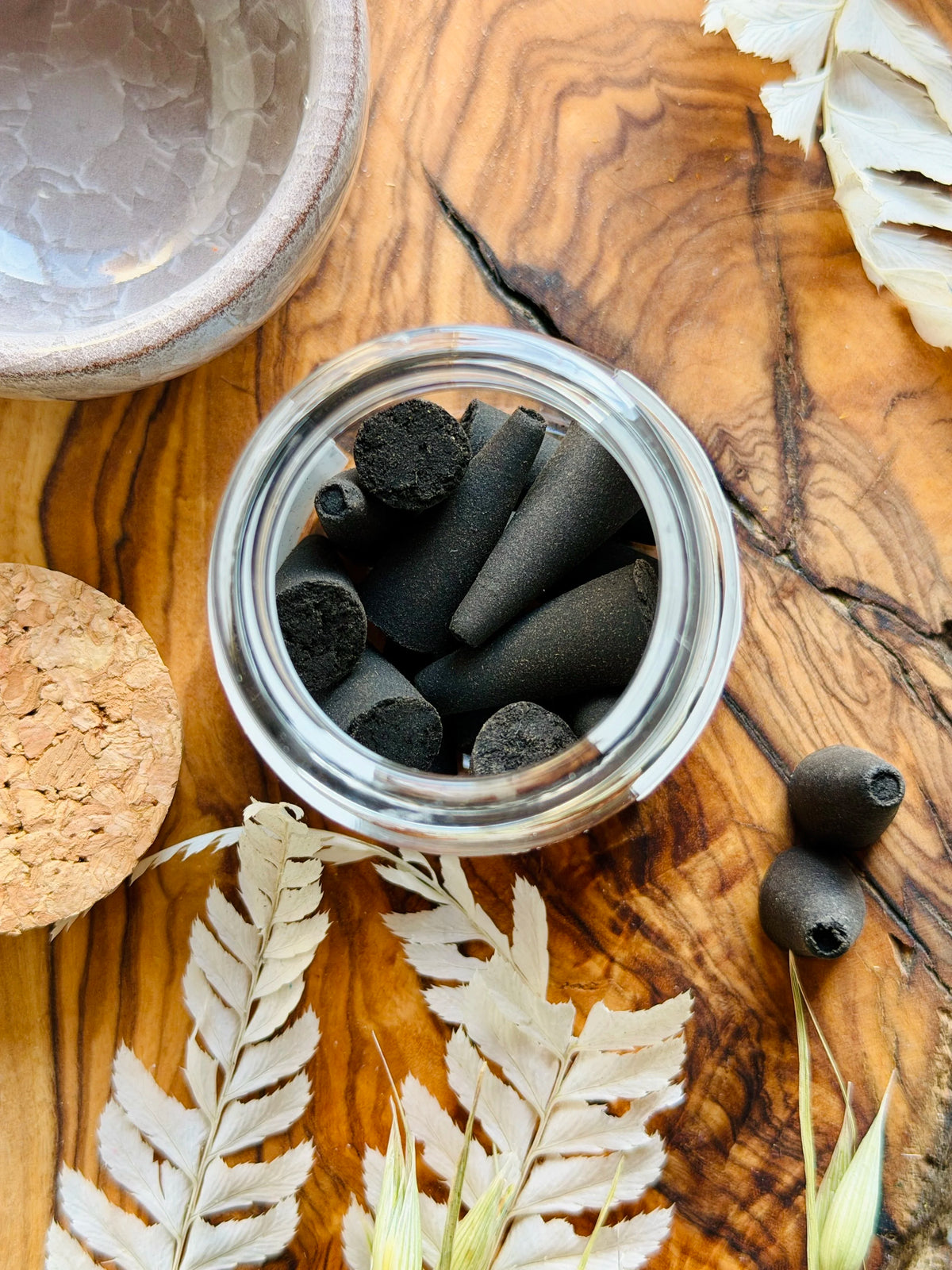 Jar of charcoal incense cones on a wooden surface with leaves and a cork lid.